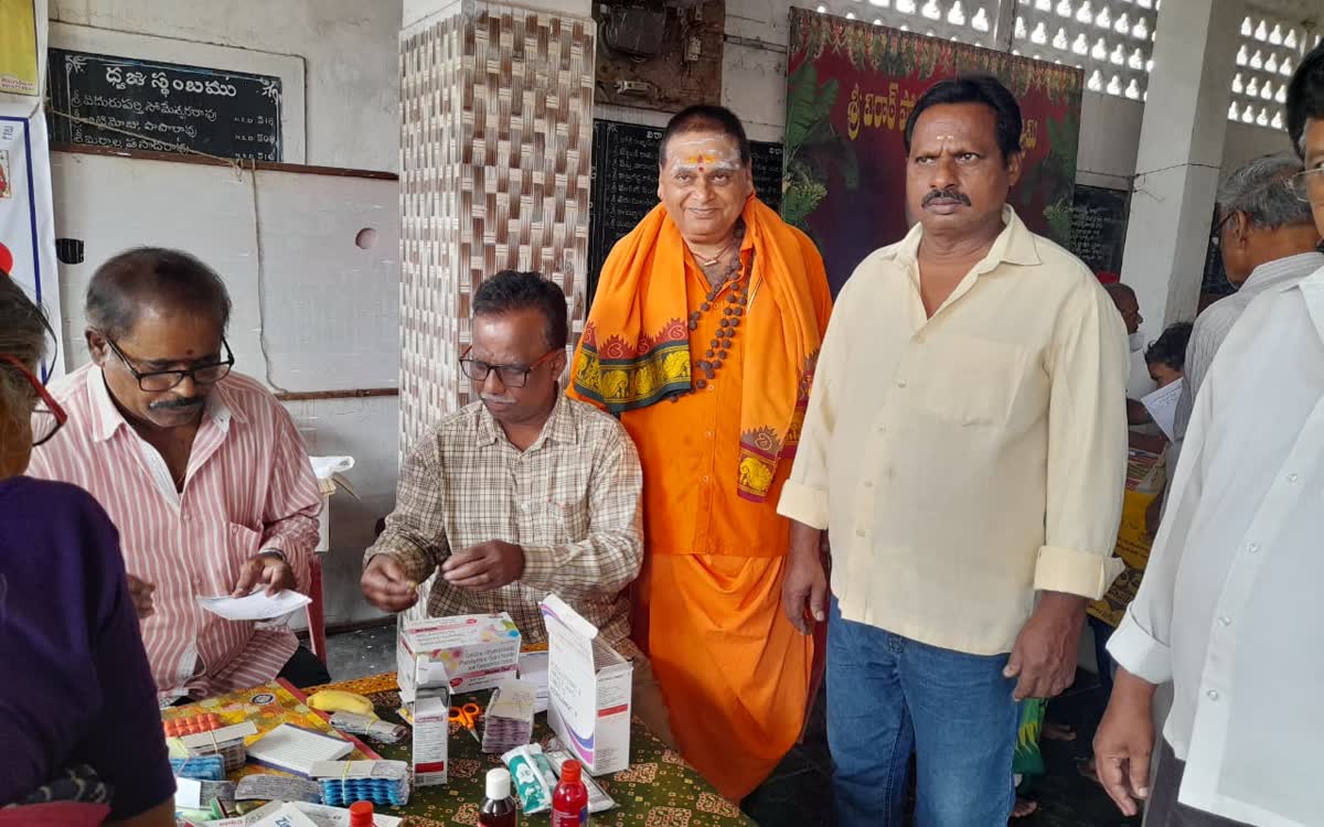 Men sorting boxes of medicine on a table at the camp while Guruji stands beside them