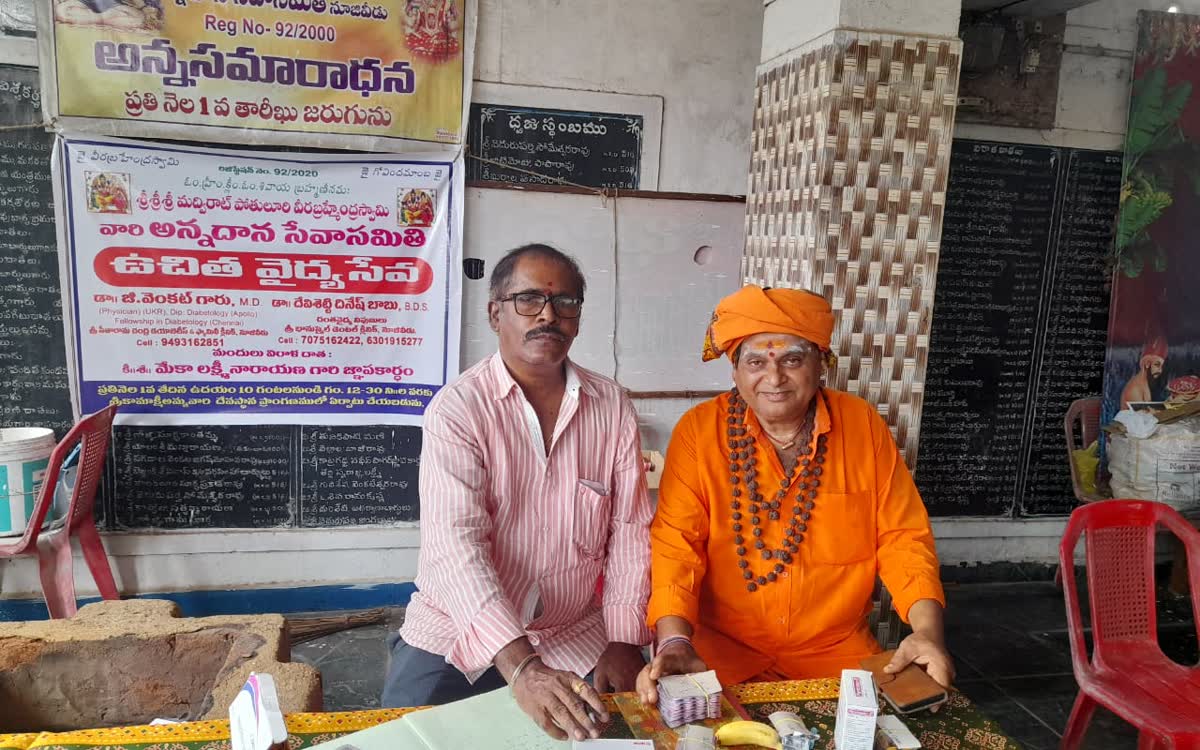 Guruji seated beside a table of medicines under a banner for the annasamaradhana