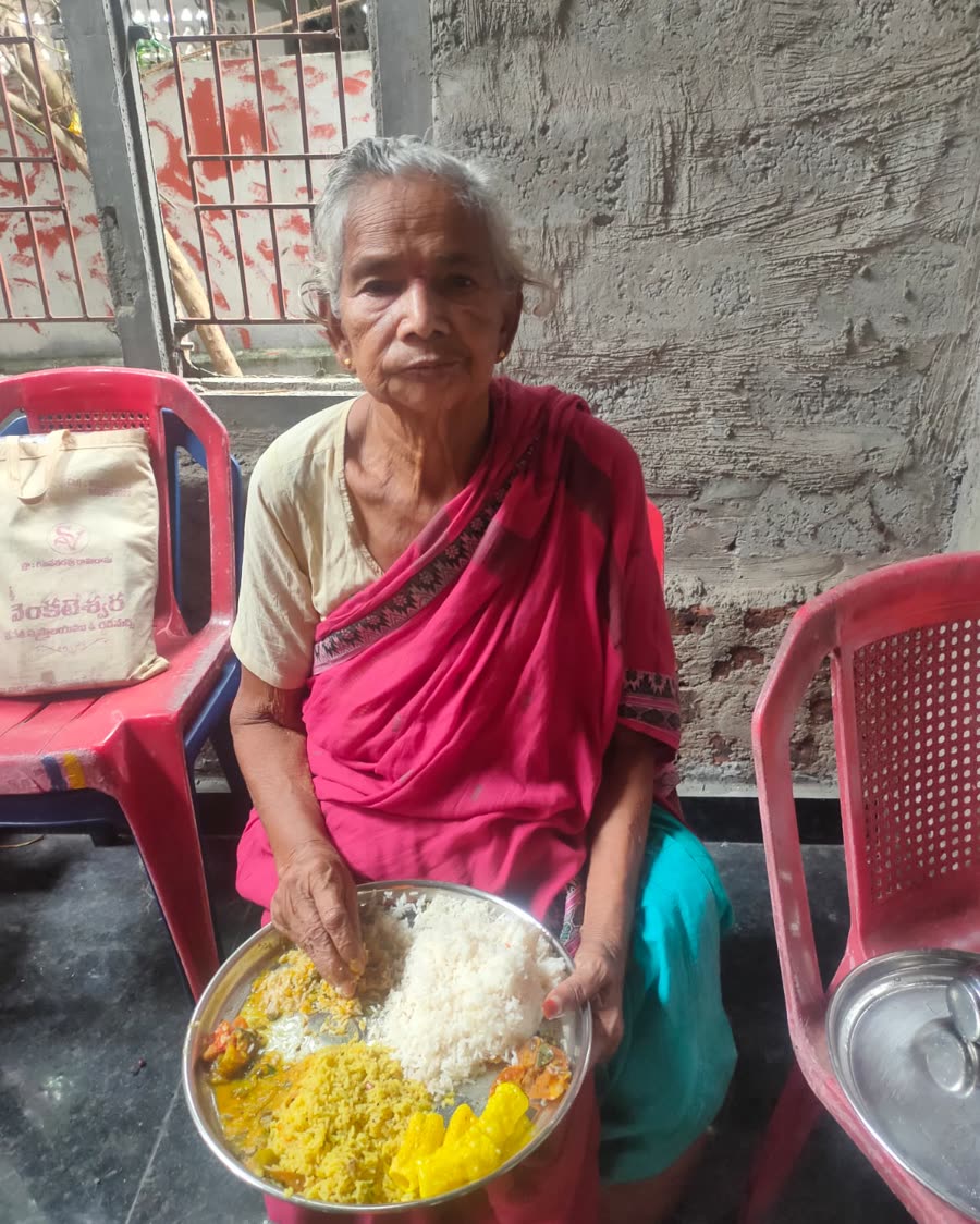 An elderly woman seated with a full plate of rice and curry