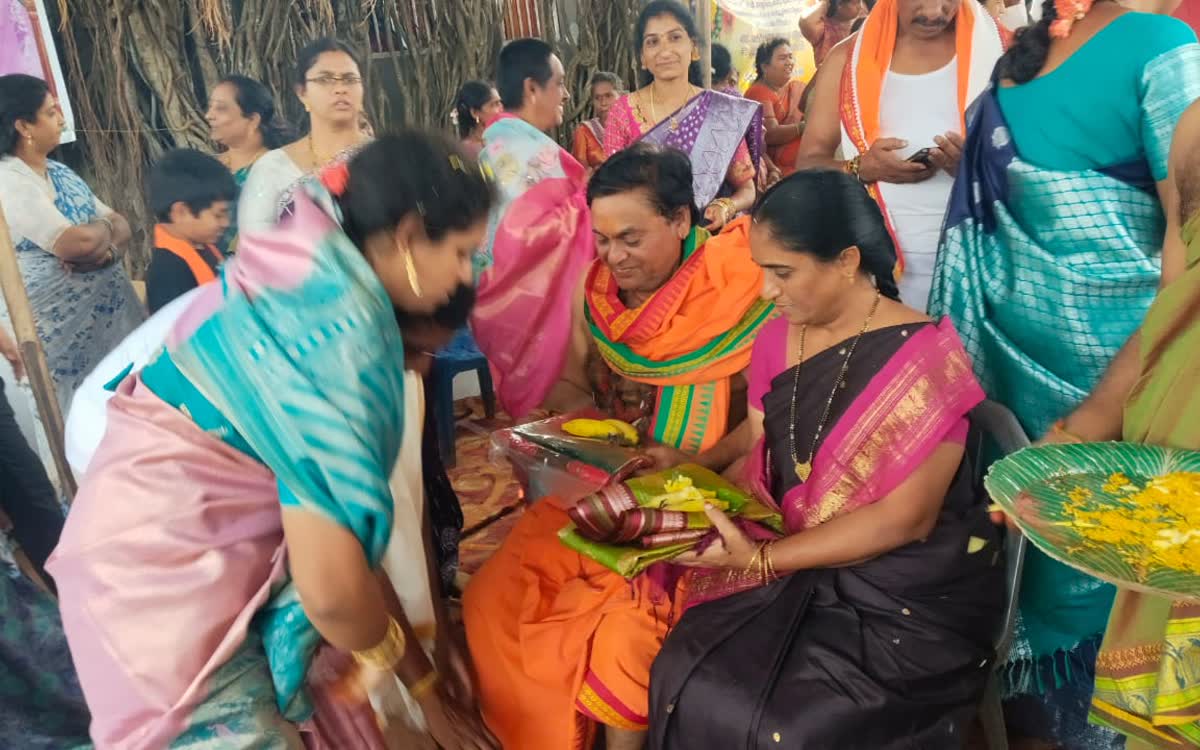 Women in saris seated close together while plates of prasadam are handed round
