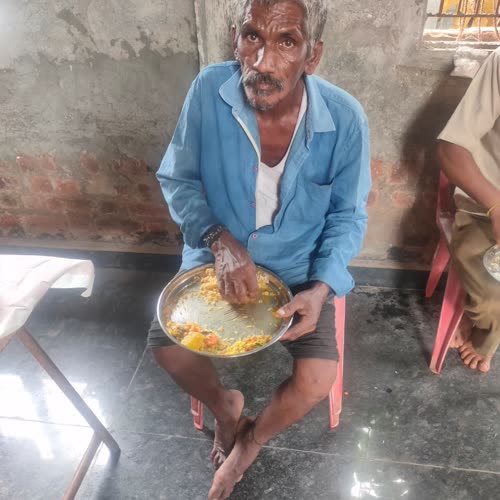 An elderly man seated on the floor, eating from his plate