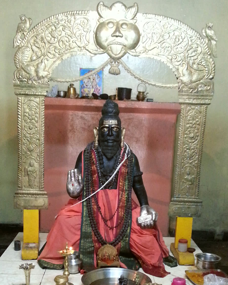 The Swamy's idol seated under a silver arch in the shrine, lamps and offerings before it